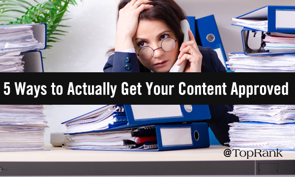 Exasperated-looking woman sitting at a desk covered in piles of paper takes a phone call.